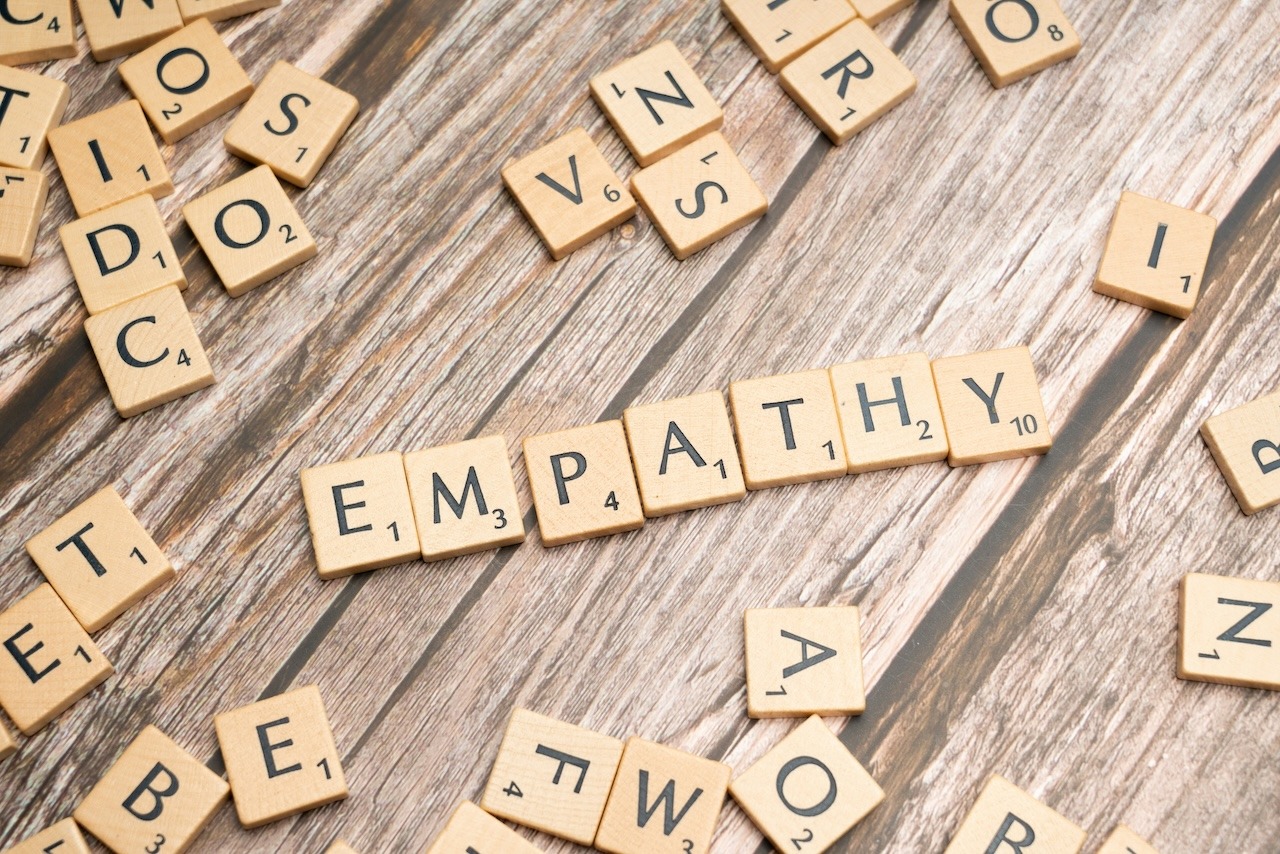 A collection of Scrabble tiles on a tabletop. In the center, the word 'empathy' is spelled out with tiles.