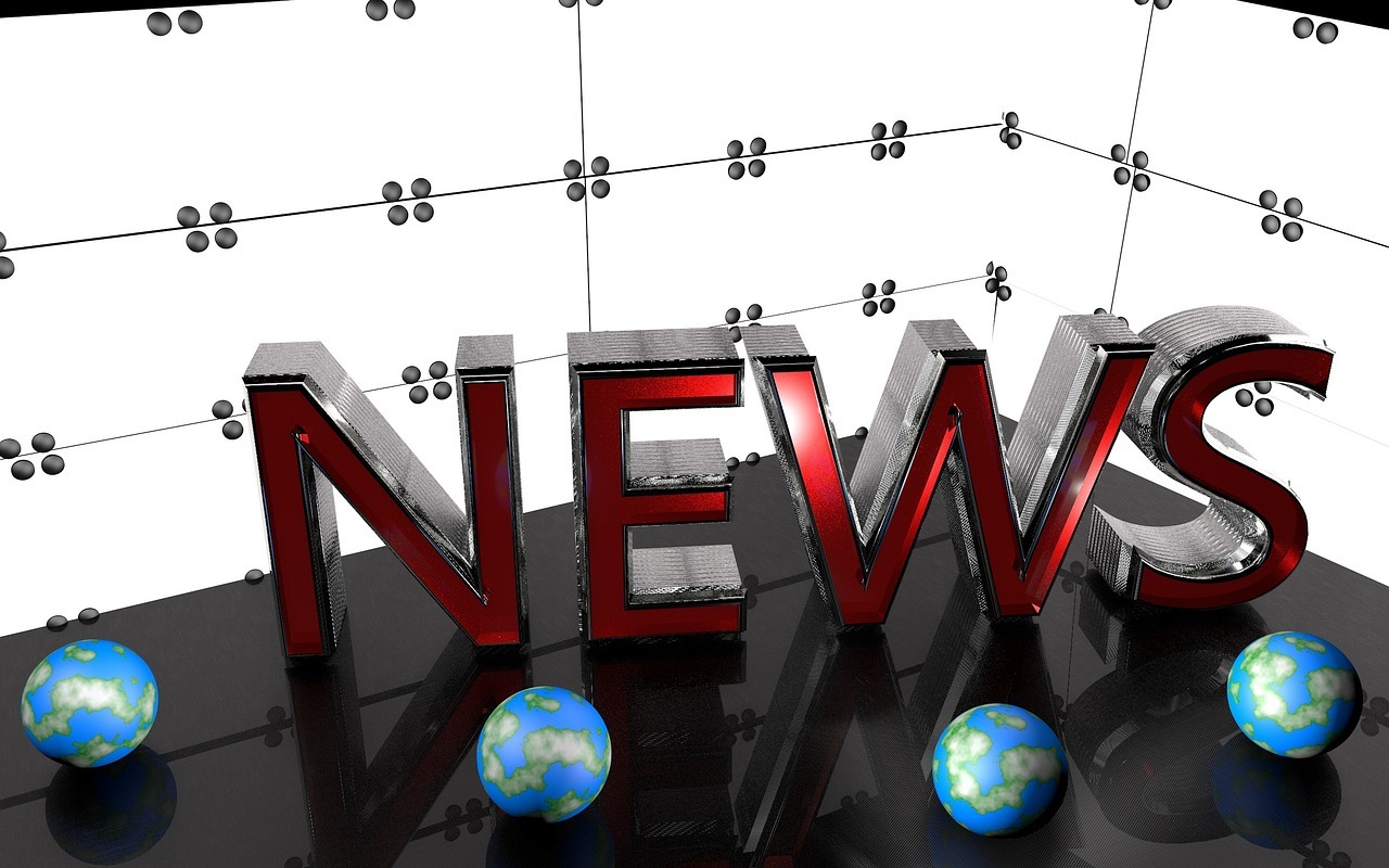 The word "news" formed in red metal, against a backdrop of white glass panels and a black desktop.