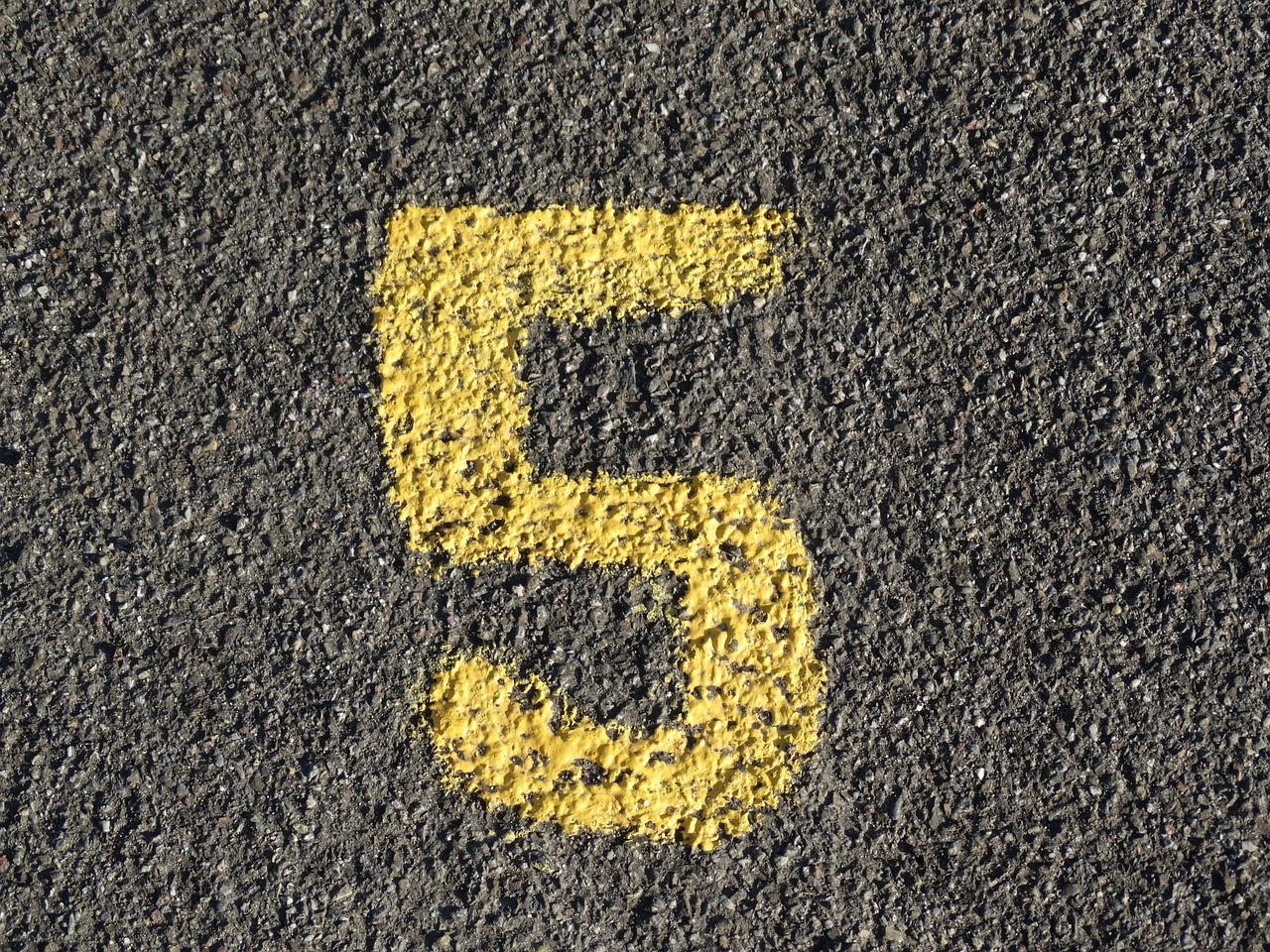 The number 5 spray painted in yellow on grey asphalt.