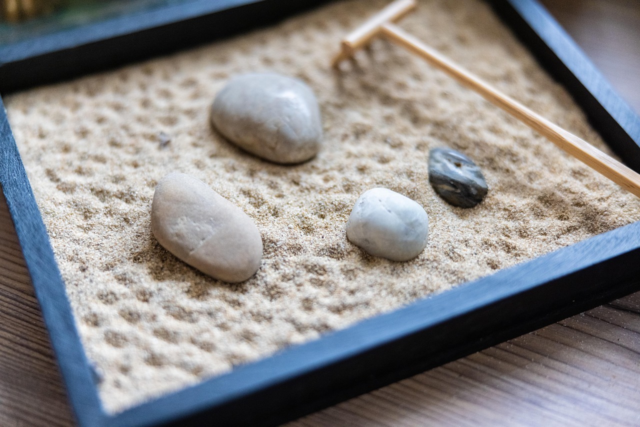 A desktop rock garden, with four rocks of different sizes, a bed of sand, and a small rake.