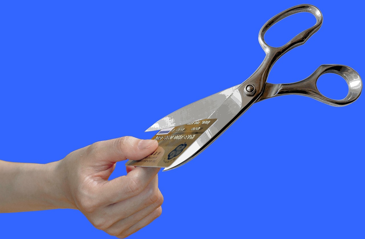 A hand holding a credit card. The card represents starting debt, and it's being cut by a pair of scissors.