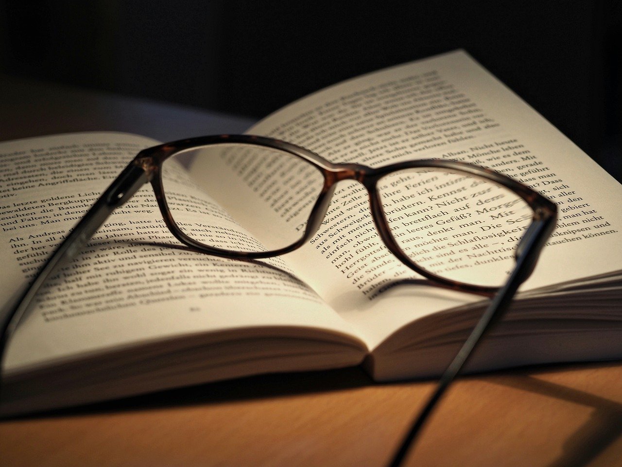 A book on a table, open to roughly the middle. A pair of glasses rests on the open pages. The reader is invited to interpret what they are reading.