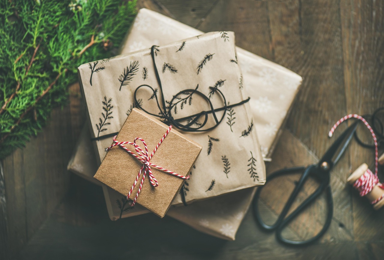 A stack of several Christmas presents seen from above, near some ribbon and a pair of scissors.
